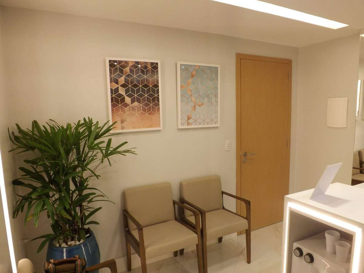 Recepção do consultório com poltronas, planta, quadros geométricos e porta de madeira